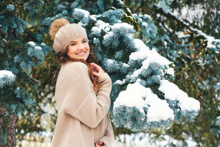 Winter portrait of beautiful woman posing in snow forest, wearing beige hat and pulloverの写真素材
