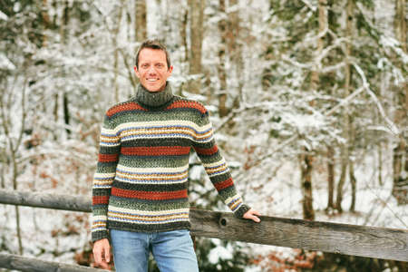 Outdoor winter portrait of middle age man in snowy forest, wearing warm knitted pulloverの写真素材
