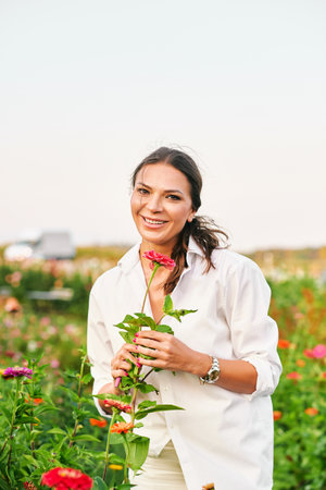 Portrait of beautiful mature woman enjoying nice day in garden, holding pink zinnia flowerの写真素材
