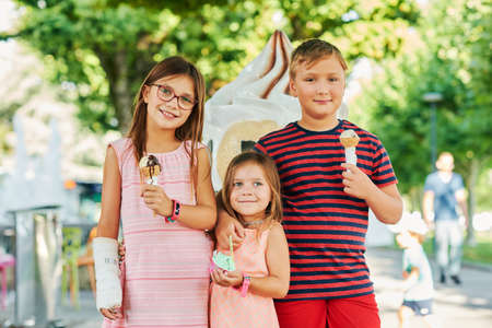 Group of 3 funny kids eating ice cream outdoors on a nice sunny day