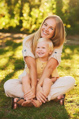Outdoor sunny portrait of happy young mother hugging adorable toddler boy, family timeの写真素材