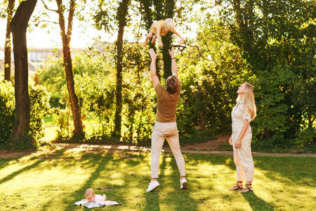 Outdoor portrait of happy family having fun in summer park, young couple with toddler boy and baby...