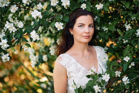 Outdoor portrait of beautiful mature woman in spring park enjoying blossoming of Jasmine flowersの写真素材