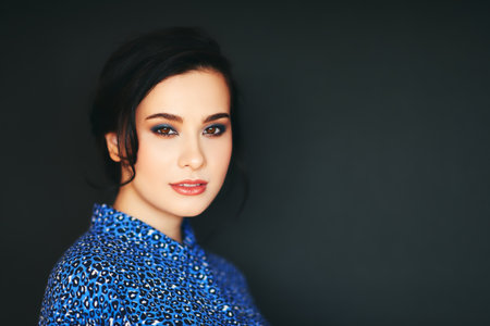 Fashion portrait of stylish young brunette woman wearing blue animal pring clothes, posing on black backgroundの写真素材
