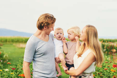 Happy young lovely family with small kids enjoing nice day in summer park or garden with blooming...