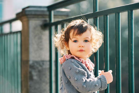 Outdoor portrait of adorable 1 - 2 year old toddler girl , wearing grey blue knitted pullver, playing in parkの写真素材