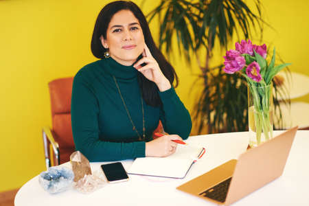 Beautiful middle age woman working in colorful cosy office, using portable laptop computer