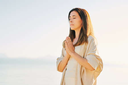 Beautiful spiritual woman meditating by the lake, wearing beige clothes