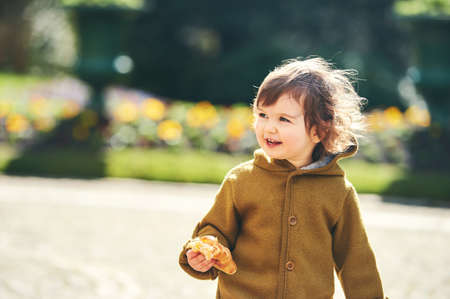 Outdoor portrait of cute 1 - 2 year old toddler kid eating croissantの写真素材