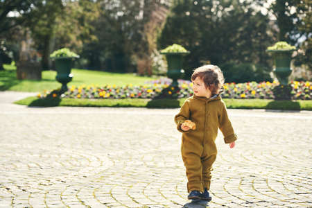 Outdoor portrait of cute 1 - 2 year old toddler kid eating croissant