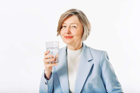 Studio portrait of middle age woman posing on white background, 55 - 60 year old female model holding glass of waterの写真素材
