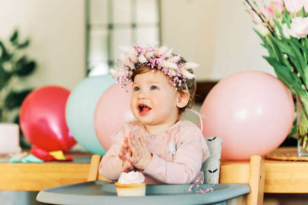 Adorable 1 year old baby girl eating cupcake, happy child sitting in a chair, tasting sweet dessert, first birthdayの写真素材