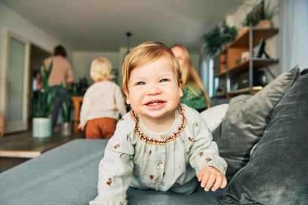 Happy young mother playing with adorable toddler girl, resting on a couch in living room