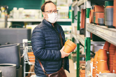 Middle age man buying pots for plants in garden center, hobby and activities. person wearing facial mask in shopping centerの写真素材