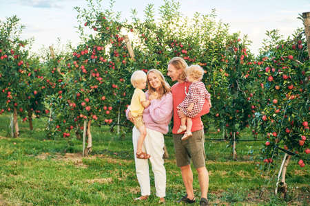 Outdoor portrait of happy young family with two little children enjoying good time in apple orchard