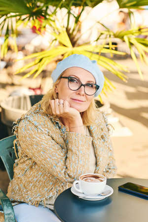 Outdoor portrait of beautiful middle age woman relaxing in outdoor cafe, drinkin coffee or cappuccinoの写真素材