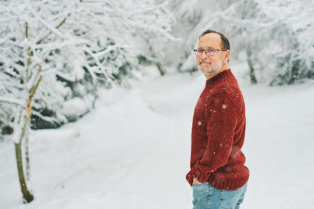 Outdoor portrait of middle age 55 - 60 year old man enjoying nice cold weather in winter forest, wearing red knitted pullover, looking back over the shoulderの写真素材
