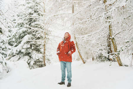 Outdoor portrait of middle age man enjoying nice day in winter forest, walking under snowfall, wearing red orange jacketの写真素材