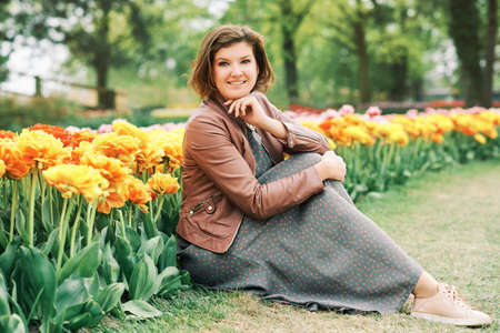 Outdoor portrait of happy young woman enjoying nice day in spring park with tulip flowersの写真素材