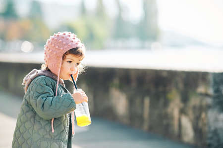 Outdoor portrait of cute little girl drinking orange juice on her morning walk