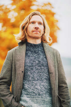 Outdoor portrait of young red haired man, wearing pullover and coat, cold foggy day