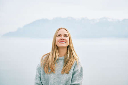 Outdoor portrait of happy beautiful young woman relaxing in mountains over the clouds, wearing grey pulloverの写真素材