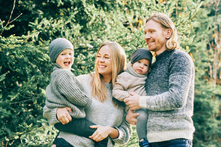 Outdoor portrait of beautiful happy young family posing in pine forest, wearing warm pullovers,...