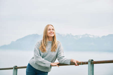 Outdoor portrait of happy beautiful young woman relaxing in mountains over the clouds, wearing grey pulloverの写真素材