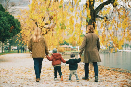 Outdoor portrait of young happy family of four, mother and father playing with children in autumn park by the lake, cold weather, back viewの写真素材