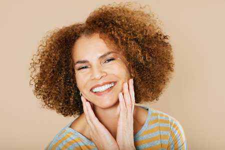 Close up studio portrait of beautiful middle age woman with curly hair, 50 - 55 year old lady posing...
