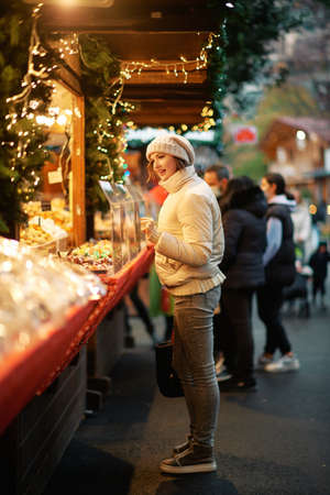 Outdoor portrait of young woman buying sweets at Christmas marketの写真素材