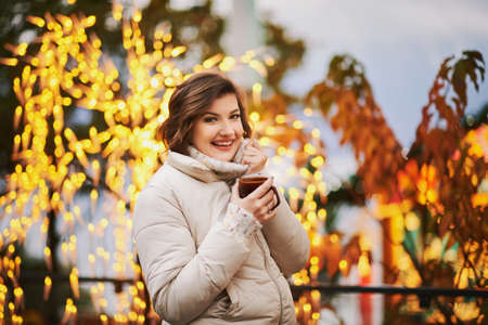Winter portrait of happy young woman drinking hot chocolate outside at Christmas marketの写真素材