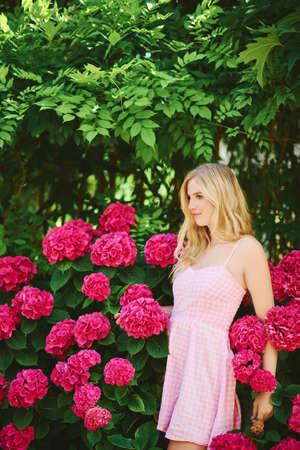 Outdoor portrait of young beautiful woman posing with hydrangea flowers in summer garden