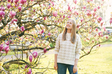 Outdoor portrait of beautiful happy model with blond hair posing next to magnolia flowersの写真素材