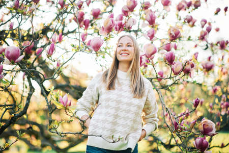 Outdoor portrait of beautiful happy model with blond hair posing next to magnolia flowersの写真素材