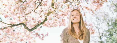 Panoramic banner background with young beautiful happy woman with blond hair, posing under blooming...
