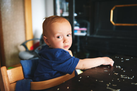 Messy baby smeared pasta on the table, toddler kid eating by himself