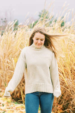 Fall portrait of young pretty girl posing outside with pampas grass, wearing warm beige pullover, windy dayの写真素材