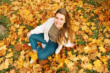 Top view autumn portrait of happy young female model girl sitting on yellow leaves, looking straight at cameraの写真素材