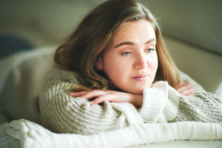 Young girl lying on couch, looking nowhere, sad emotionsの写真素材