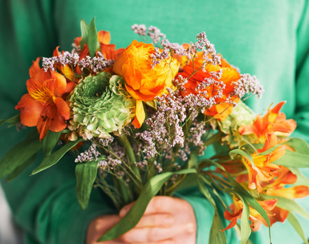 Close up portrait of beautiful green and orange ranunculus and alstroemeria bouquet holding by a personの写真素材