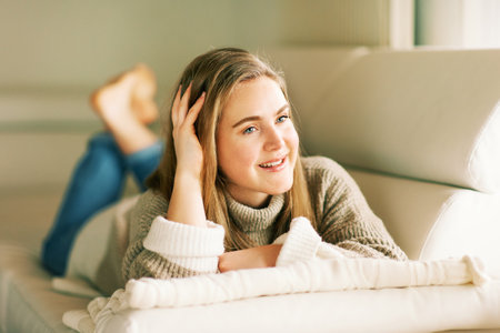 Indoor portrait of young cute 20 year old girl lying on couch, wearing warm pulloverの写真素材