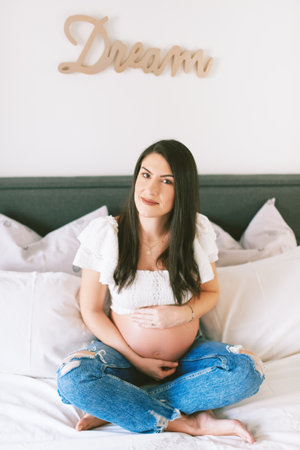 Indoor portrait of beautiful young pregnant woman resting on bed