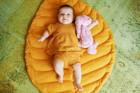 Portrait of adorable 6 months old baby lying on playing blanket, holding pink bunny toy, top view