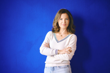 Portrait of pretty 40 year old woman posing next to bright blue wall