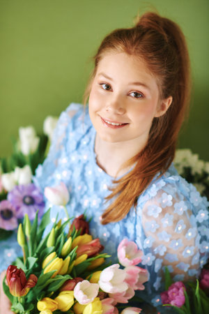 Portrait of pretty young 15 - 16 year old red-haired girl surrounded by many spring flowers posing...