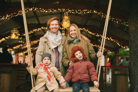 Outdoor portrait of happy young family at Christmas market, parents with 2 little children enjoying holidays, travel with kidsの写真素材
