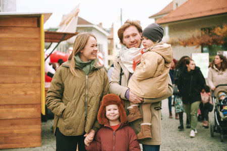 Outdoor portrait of happy family of four, young couple with 2 little children, cold weather, fall timeの写真素材