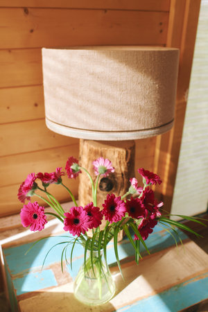 Bright pink gerbera flowers in a glass vase placed on end tableの写真素材