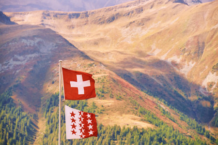 Swiss flag and flag of canton of Valais against swiss alpine mountainの写真素材